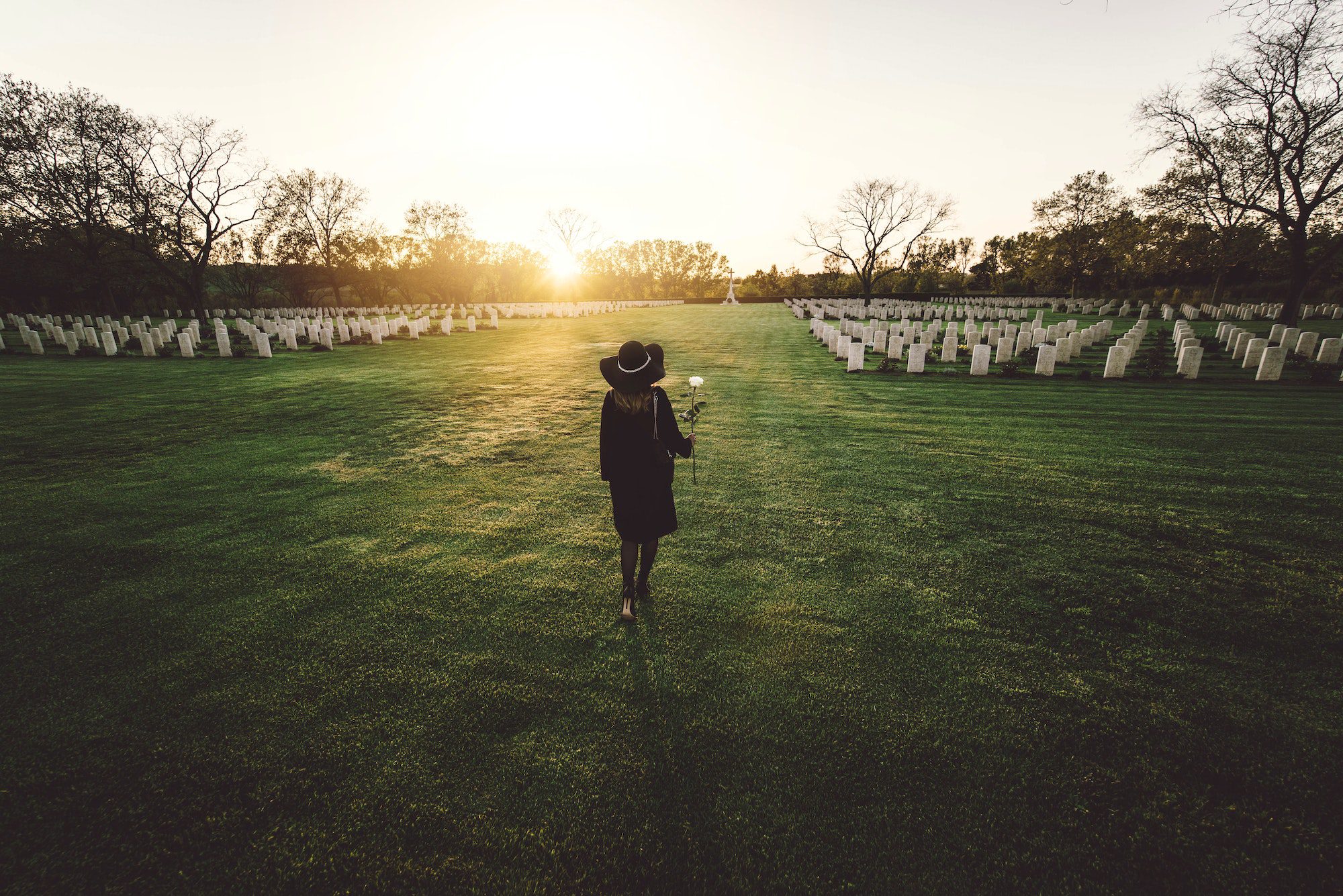 Sad woman in the cemetery holding bouquet of roses in her hand