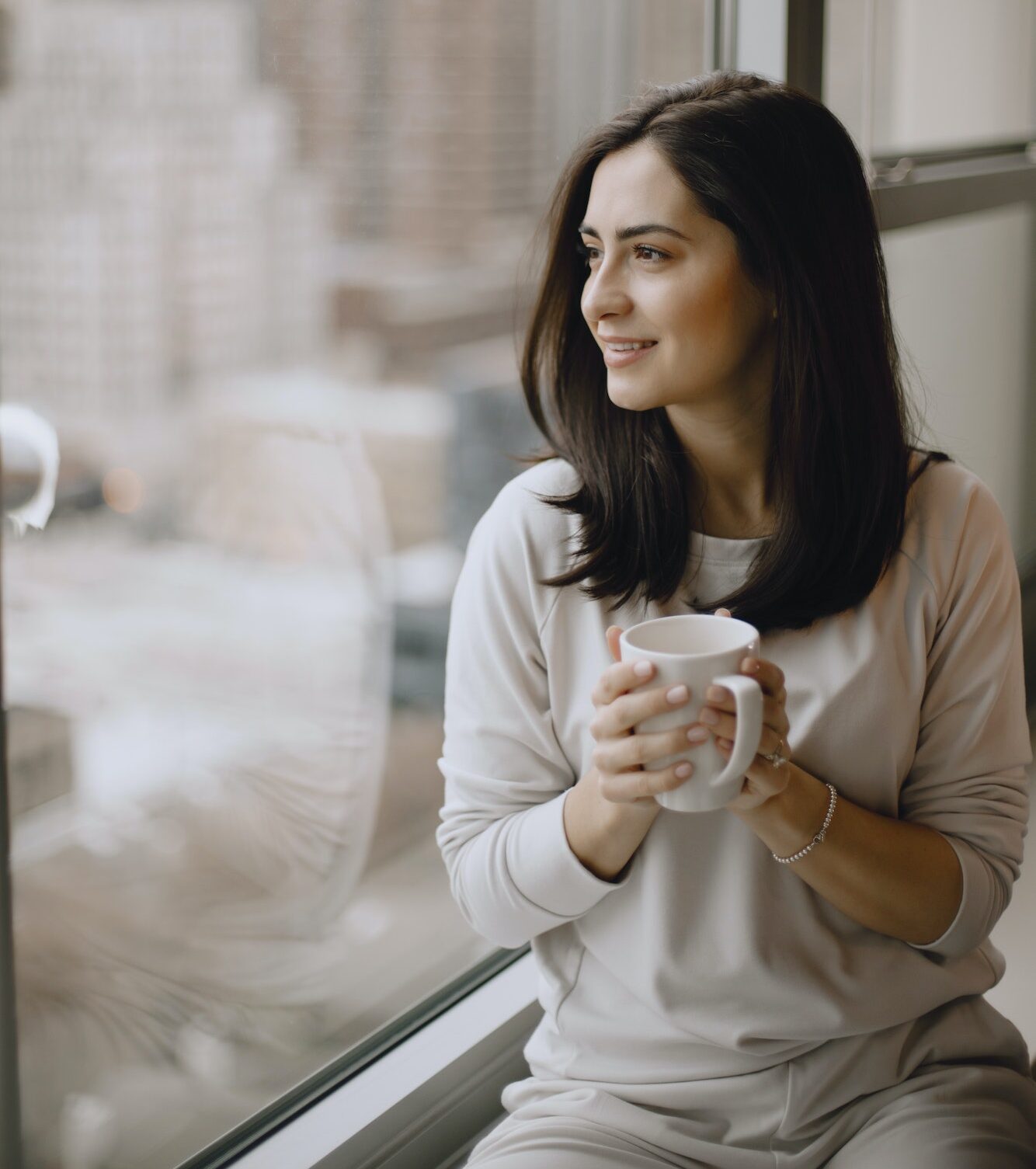 Brunette sitting on a windowsill and drinks a coffee