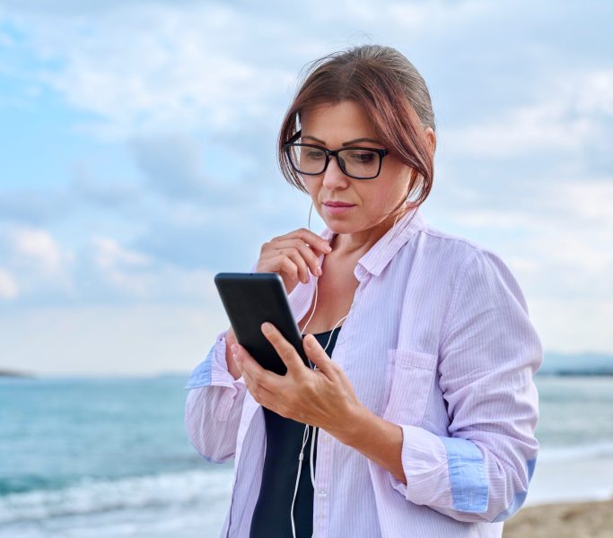 Middle age sad serious woman in headphones with smartphone outdoor.